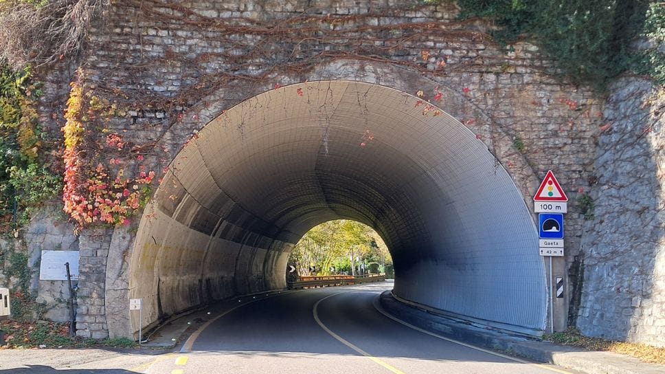 Il cartello che indica dove dovrebbe essere scavato il piccolo tunnel ciclopedonale, a margine della galleria utilizzata dalle auto