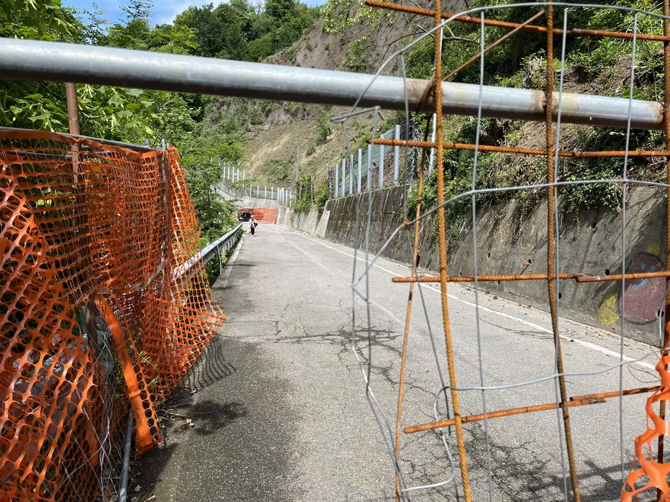 Il buco nella rete che impedisce l’accesso alla strada su cui è arrivata la frana (e in lontananza una persona che la percorre)